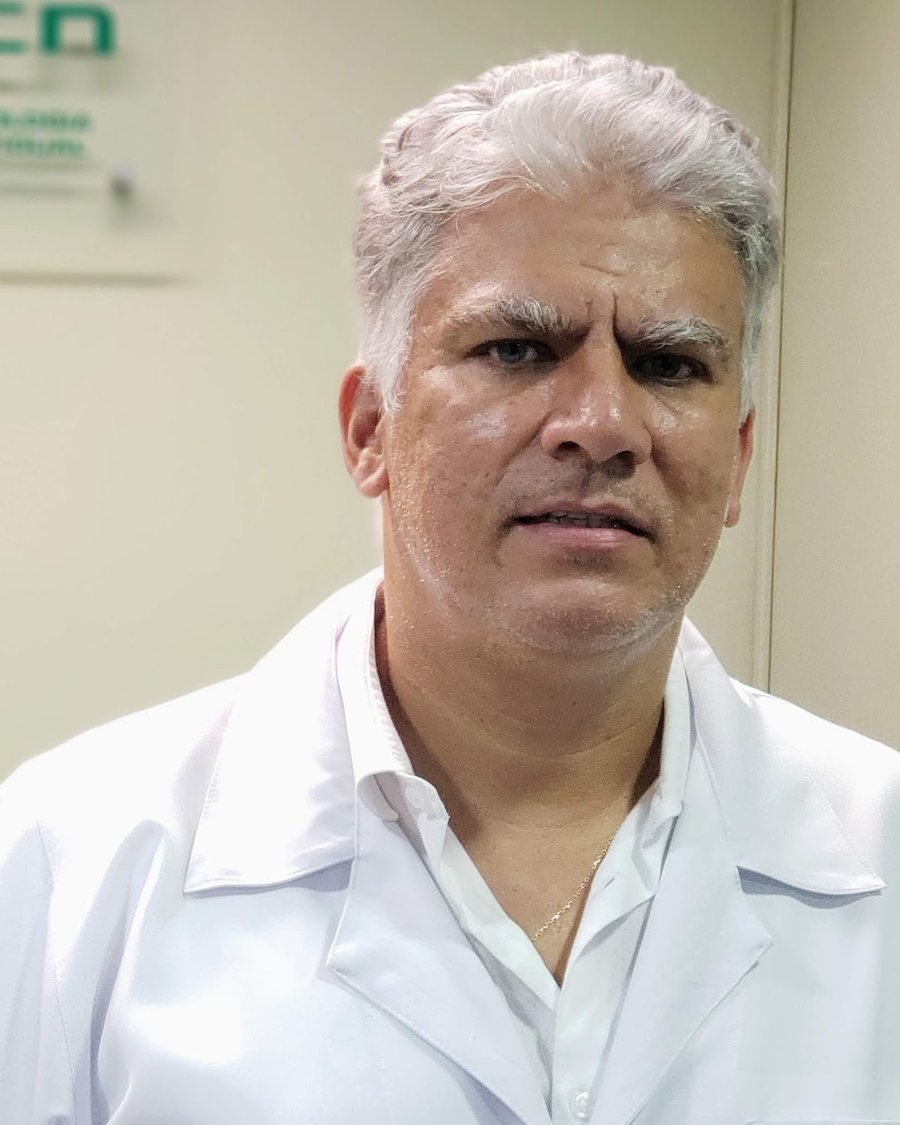 Dr. Carlos Alberto Silva Junior, de jaleco branco, em frente à placa da clínica
